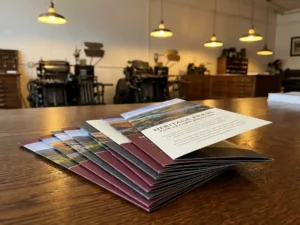 Stapel elegante drievoudige brochures uitgewaaierd op gepolijst houten bureau in traditionele drukkerij met professionele apparatuur op achtergrond