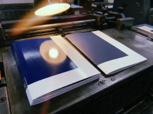 Glanzende brochure met UV-coating naast matte versie op drukpers, toont verschil in glans en kleurdiepte